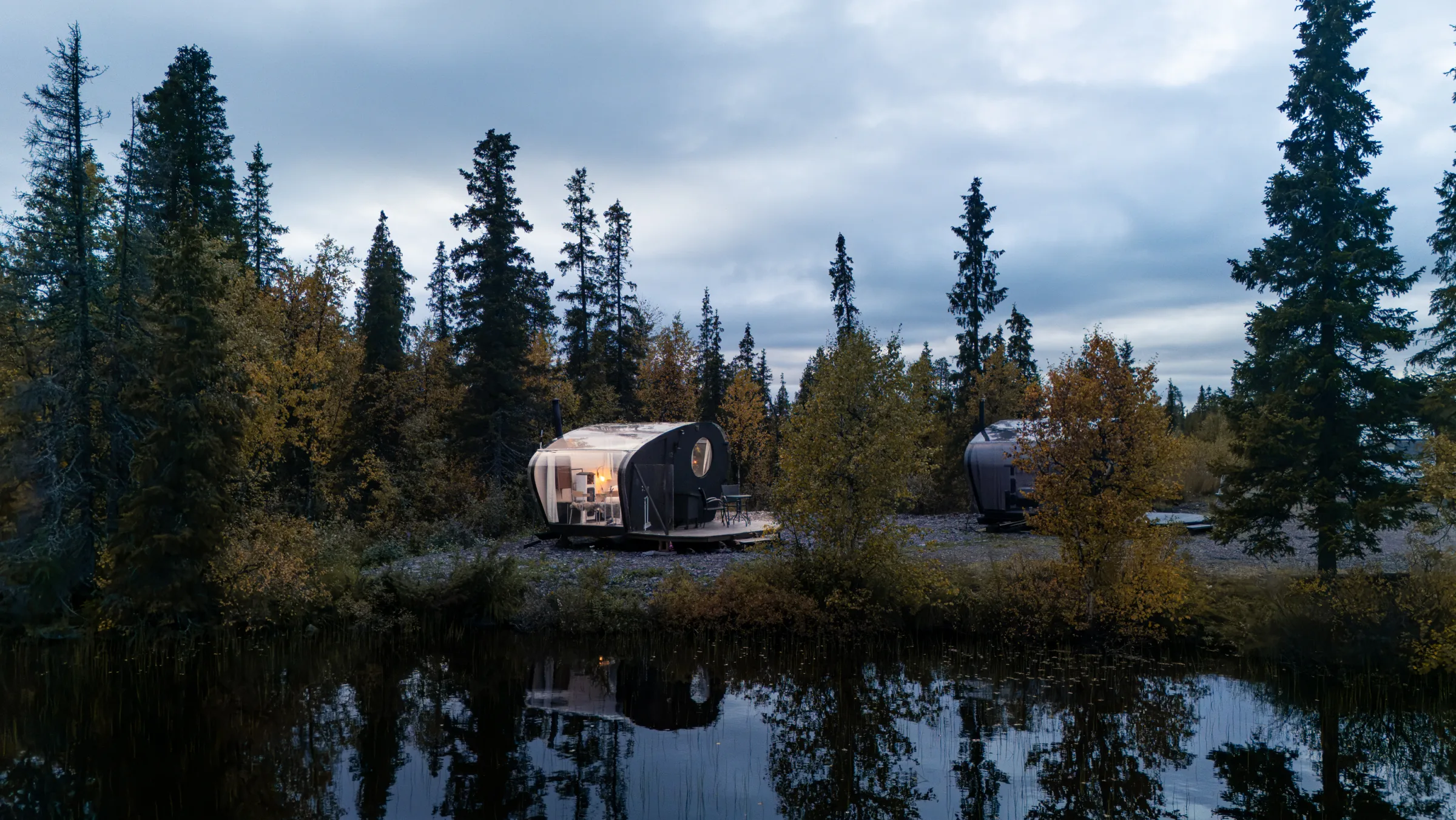 The cabin among the trees on the lake shore at dusk